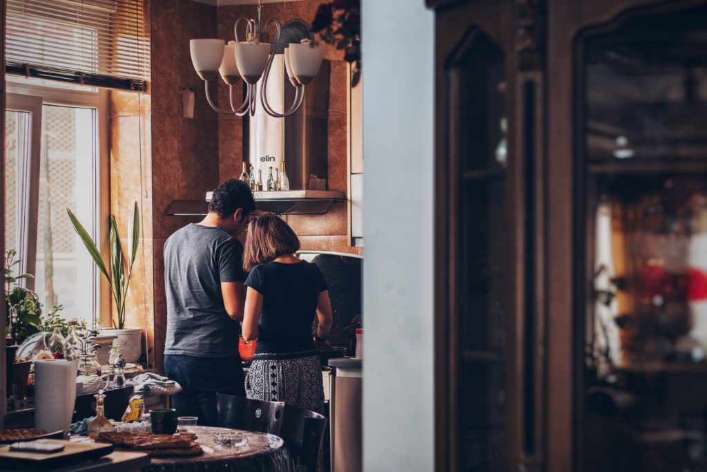 A man and woman standing and cooking over a gas range stove in their rustic apartment.